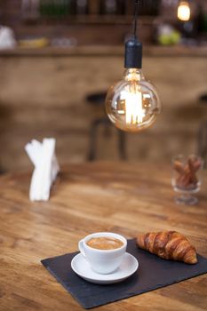 Fresh roasted coffee in a white coffee cup with tasty croissant on a vintage pub. Strong coffee. Parisian dessert.