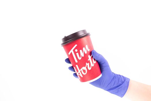 Nurse hand in medical glove holding a Tim Hortons Large Cup of Coffee. Red Tims coffee cup. Gatineau, Quebec, Canada August 4, 2022.