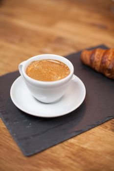 Freshly roasted coffee in a white cup served with tasty croissant. Coffee aroma. Delicious croissant