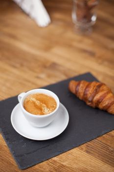 Breakfast with espresso cup of hot coffee and croissant on a black stone plate. Coffee aroma.