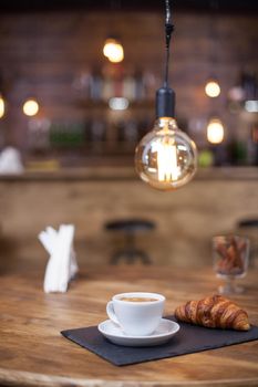 Tasty cup of latte macchiato with delicious croissant in a vintage coffee shop. Wooden table. Blurred background.