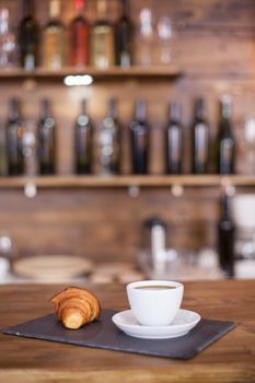 Delicious coffee and tasty croissant with blurred wine bottles in the background. Old wine. Delicious breakfast.