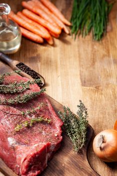 Raw meat served with vegetables and herbs decorated on rustic wooden board.