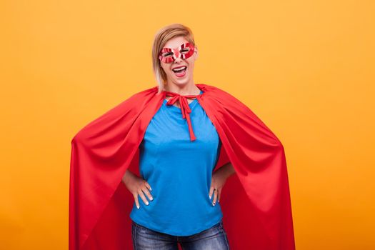 Mother dressed like superheros laughing at the camera over yellow background. Super powers. Red mask. Red cape.