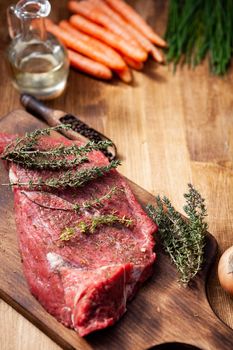 Raw meat from the butcher seasoned with rosemary,salt and pepper next to virgin olive oil and carrots. Green vegetables.