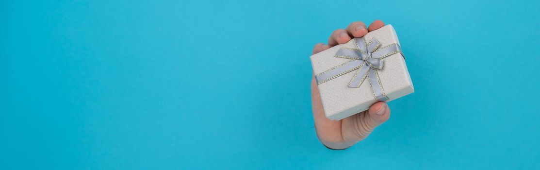 A woman's hand sticks out of a blue paper background and a gift box. Widescreen