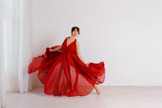 Dancer in a red flying dress. Woman ballerina dancing on a white studio background.