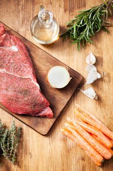 Raw steak with garlic and carrots on wooden background. Food preparation. Natural ingredients.