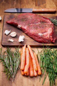 Big filet of red meat on rustic cutting board next to fresh vegetables and chef knife. Green herbs.