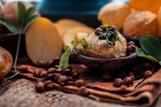 Famous Indian & Asian street food dish i.e. Panipuri snack in a clay bowl along with its flavored spicy water in another clay vessel. Entire consisting raw ingredients present on the surface.