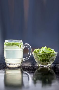 Close up of glass mug on wooden surface containing aloe vera detox drink in along with its entire raw ingredients with it. Vertical shot with blurred background.