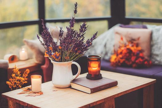 3D render of Autumn hygge home decor arrangement, concept of hygge and coziness, burning white fragrance candle on tray and lavender branches in a bottle vase on table at cozy home