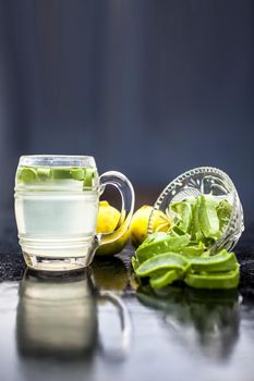Close up of glass mug on wooden surface containing aloe vera and lemon juice detox drink along with its entire raw ingredients with it. Vertical shot with blurred background.