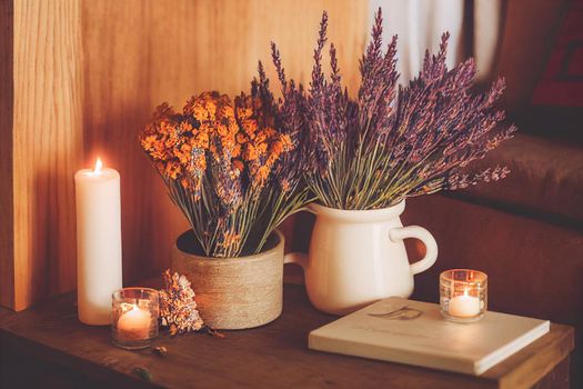 3D render of Autumn hygge home decor arrangement, concept of hygge and coziness, burning white fragrance candle on tray and lavender branches in a bottle vase on table at cozy home