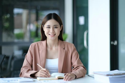 Young Asian businesswoman sitting at their desk and take notes using laptop in the office..