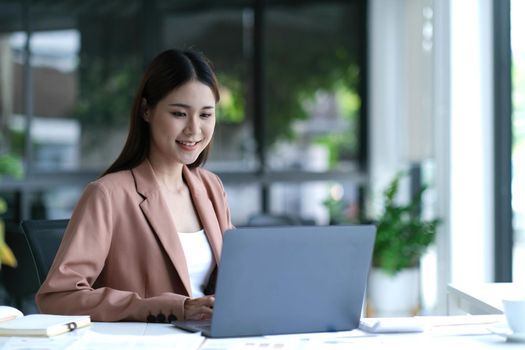 Charming asian businesswoman sitting working on laptop in office..