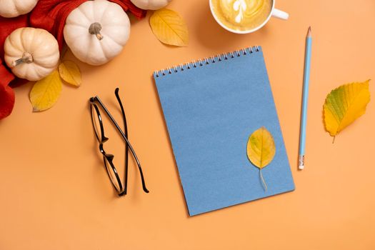 Flat lay blank notepad for text next to pumpkins and autumn leaves with coffee cup. Autumn theme mockup.