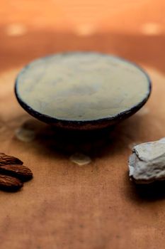 Fuller's earth face mask in a clay bowl on brown fabric's surface along with some milk and almonds. For softer skin.
