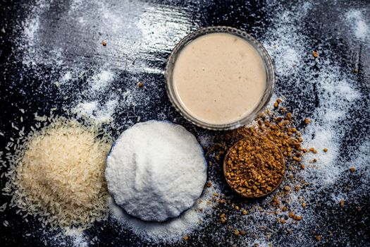 Hair growth remedy of rice flour water and fenugreek/coriander/parsley seeds powder on wooden surface and its paste in a glass bowl with some rice flour spread on the surface. Horizontal shot.