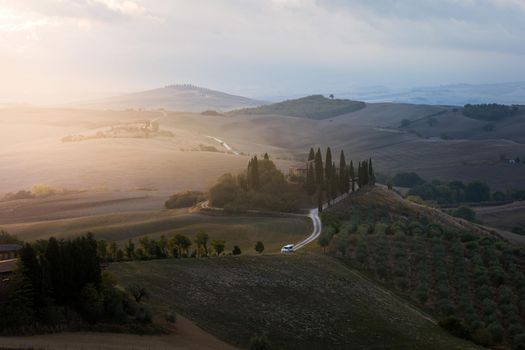Well known Tuscany landscape with grain fields, cypress trees and houses on the hills at sunset. Summer rural landscape with curved road in Tuscany, Italy, Europe