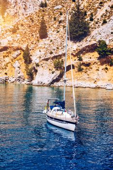 Yacht anchoring in crystal clear turquoise water in front of the tropical island, alternative lifestyle, living on a boat. View of yacht at anchor on turquoise water, showing luxury, wealth.