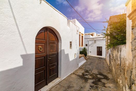 Narrow street in Lindos town on Rhodes island, Dodecanese, Greece. Beautiful scenic Lindos old ancient white houses with flowers. Famous tourist destination in South Europe. Lindos, Rhodes, Greece.