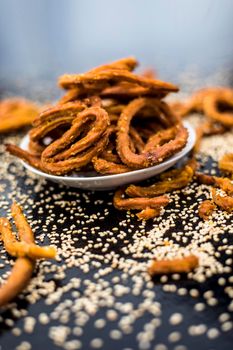 Famous Indian snack in a glass plate on the wooden surface along with raw sesame seeds or til spread on the surface.