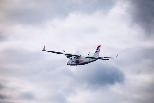 Light small plane flies against the background of white rainy clouds not high above the ground. Light aircraft on the air. A small tourist plane on an isolated white rainy clouds.
