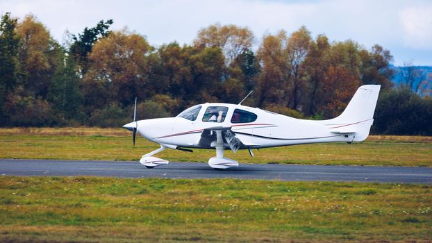 Light small plane flies against the background of a forest not high above the ground. Light aircraft on the air. A small tourist plane on an isolated white rainy clouds.