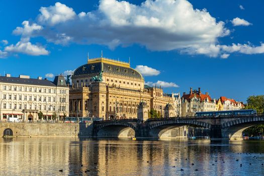 National Theatre located in Prague, Czech Republic on the Vltava River. Legion bridge on river Vltava. National Theatre (Narodni Divadlo) on embankment in sunbeams of evening sunset sunlight. Prague