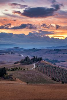 Well known Tuscany landscape with grain fields, cypress trees and houses on the hills at sunset. Summer rural landscape with curved road in Tuscany, Italy, Europe