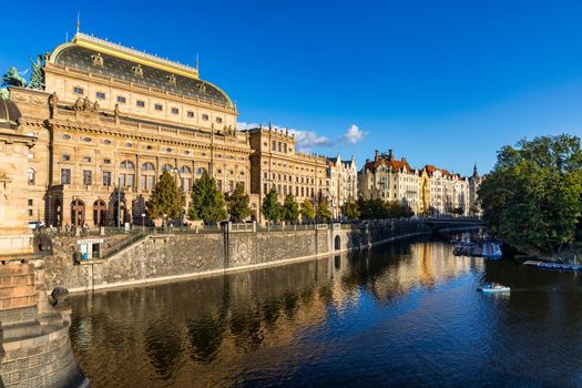 National Theatre located in Prague, Czech Republic on the Vltava River. Legion bridge on river Vltava. National Theatre (Narodni Divadlo) on embankment in sunbeams of evening sunset sunlight. Prague