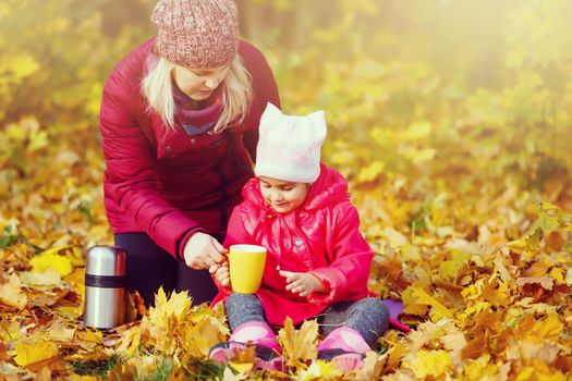 On an autumn walk Mom pours warm tea from her thermos to her daughters. The concept of a family walk.