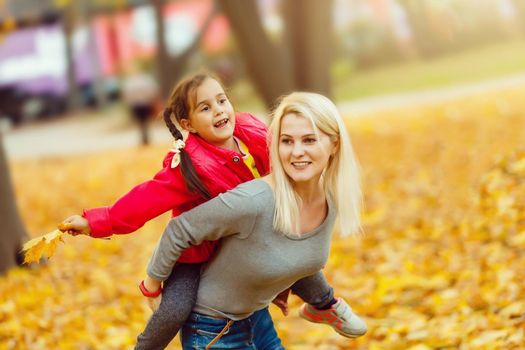 Happy family: mother and child little daughter play cuddling on autumn walk in nature outdoors