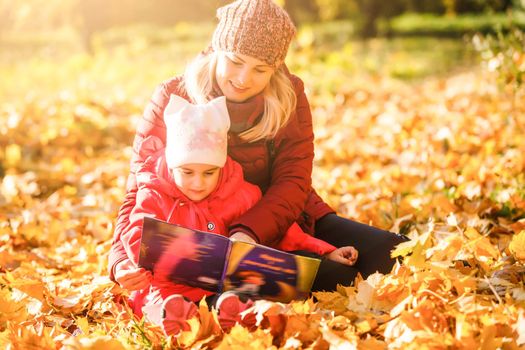 Cute little girl is reading a book outdoors autumn