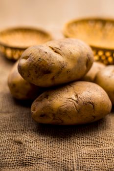 Close up shot of potato or aloo or alu on jute bag surface along with two vegetable and fruit hampers.