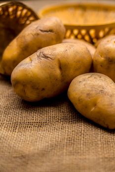 Close up shot of potato or aloo or alu on jute bag surface along with two vegetable and fruit hampers.