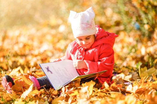 Cute little girl is reading a book outdoors autumn