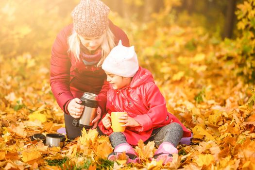 On an autumn walk Mom pours warm tea from her thermos to her daughters. The concept of a family walk.