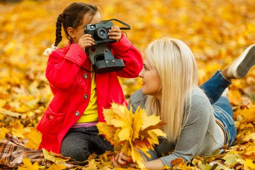 Young mother playing with her daughter in autumn park.