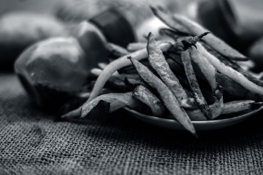 Fresh fired French fries of along with sprinkler of black pepper and salt on jute bag's surface and some raw potato also.