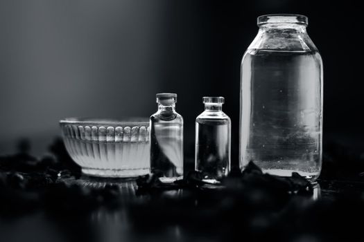 Close up of castor oil, tea tree oil, and some coconut oil in bottles on the wooden surface along with some raw honey and rose petals also present on the surface.