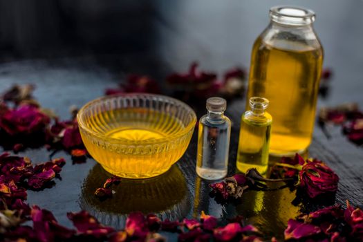 Close up of castor oil, tea tree oil, and some coconut oil in bottles on the wooden surface along with some raw honey and rose petals also present on the surface.