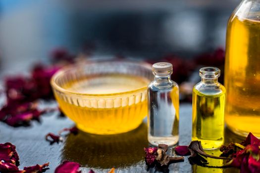 Close up of castor oil, tea tree oil, and some coconut oil in bottles on the wooden surface along with some raw honey and rose petals also present on the surface.