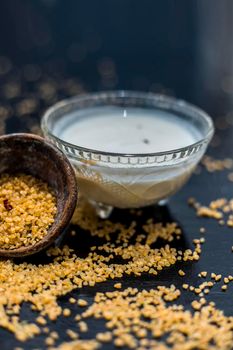 Curd or yogurt and oats face mask on the woodne surface in a glass bowl along with some raw oats in a black colored clay bowl and some spread on the surface. To Exfoliate Your Skin.