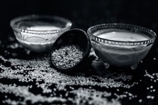 Curd or yogurt and oats face mask on the woodne surface in a glass bowl along with some raw oats in a black colored clay bowl and some spread on the surface. To Exfoliate Your Skin.