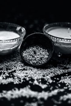 Curd or yogurt and oats face mask on the woodne surface in a glass bowl along with some raw oats in a black colored clay bowl and some spread on the surface. To Exfoliate Your Skin.