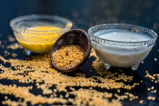 Curd or yogurt and oats face mask on the woodne surface in a glass bowl along with some raw oats in a black colored clay bowl and some spread on the surface. To Exfoliate Your Skin.