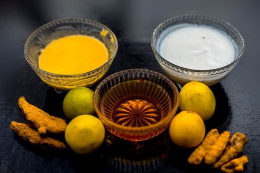 Face mask of lemon juice, honey, and curd along with some raw turmeric well mixed in a glass bowl along with entire raw ingredients on the wooden surface for acne-prone skin and blemishes.