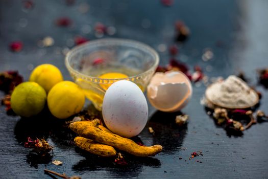 Face mask of lemon juice, honey, and curd along with some raw turmeric well mixed in a glass bowl along with entire raw ingredients on the wooden surface for acne-prone skin and blemishes.